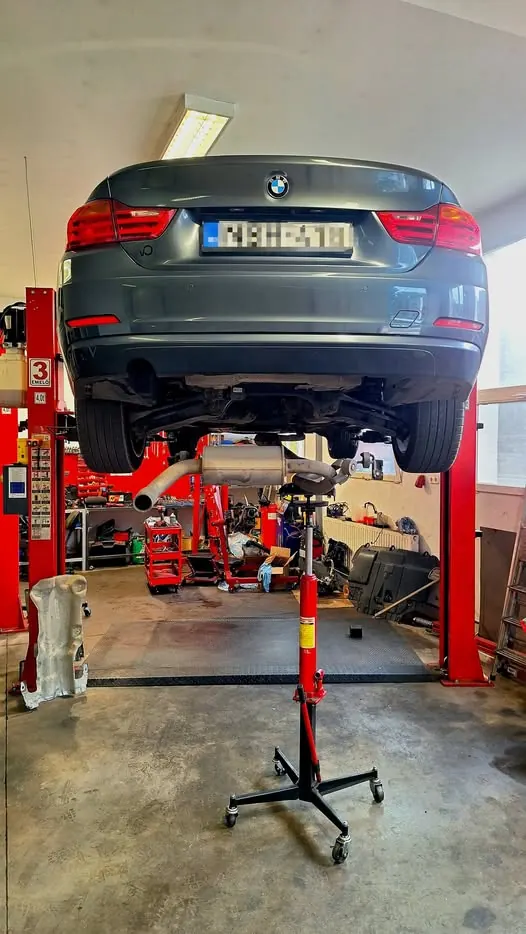 Szürke BMW emelőn, alatta hajtóműemelő a kardántengely kiszereléséhez
